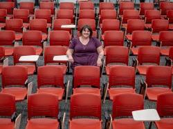 A student sits in the center of a lecture hall filled with red chairs.